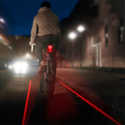 Cycliste de nuit dont le feu arrière projette deux lignes laser au sol