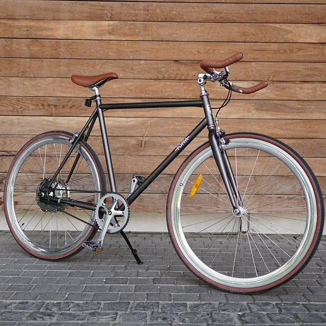 Vélo de ville noir à selle et poignées en cuir, photographié de profil devant un bardage en bois