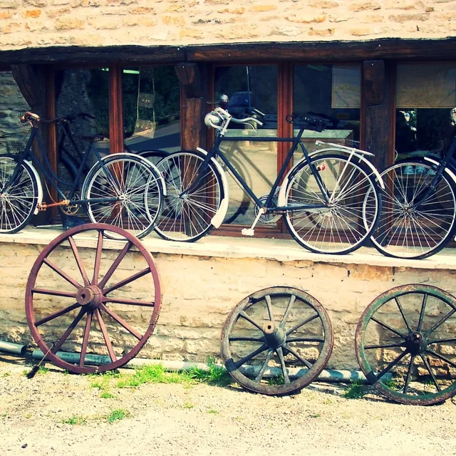 Vélos anciens alignés à la vente devant une maison en pierre, roues en bois posées au sol