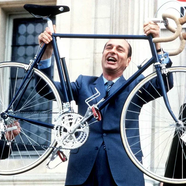 Un homme en costume brandit un vélo de course bleu à bout de bras