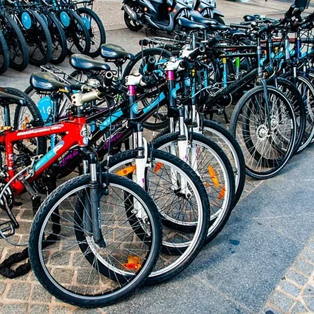 Rangée de vélos d'occasion serrés les uns contre les autres sur des pavés, devant des scooters garés