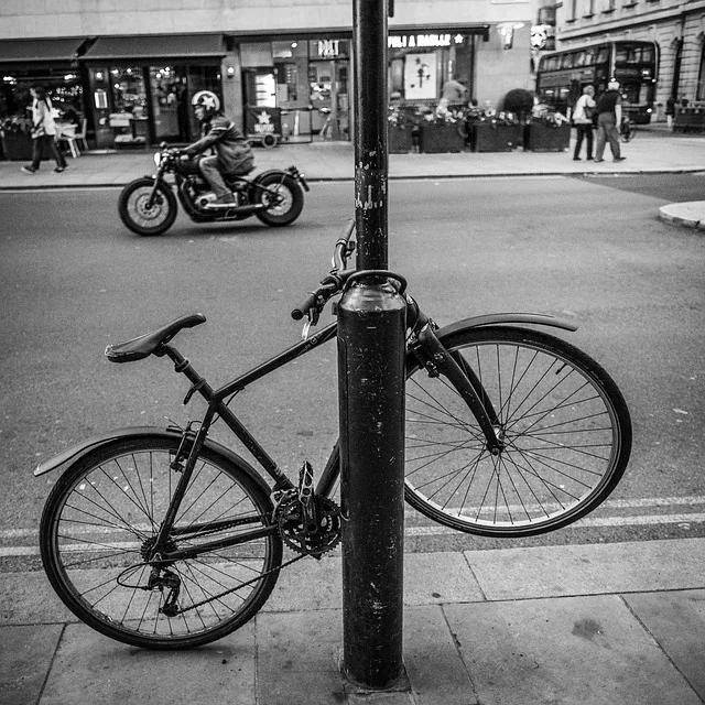 Vélo de ville attaché à un poteau de trottoir dans une rue commerçante, photographié en noir et blanc